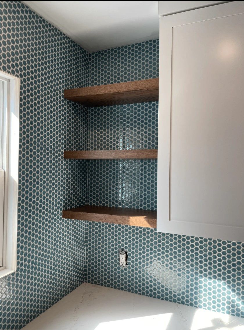 Corner with blue tiled wall, three wooden shelves, and a white cabinet.