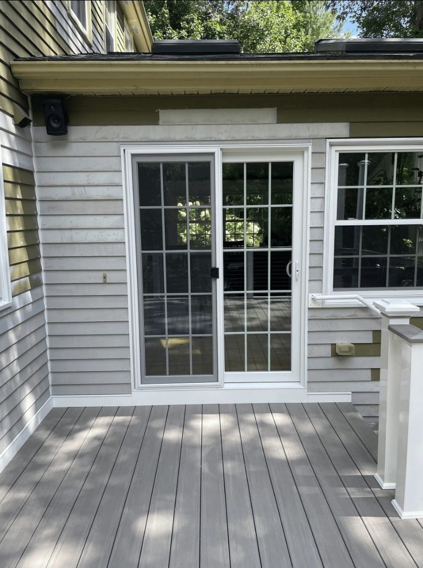 Sliding glass door and window on a light gray clapboard house, with a gray deck.