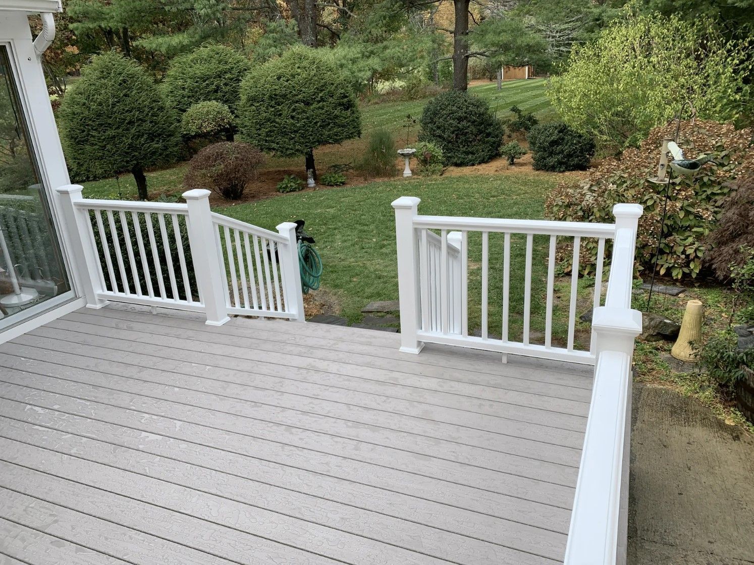 A gray deck with white railing overlooks a green lawn and trimmed bushes.