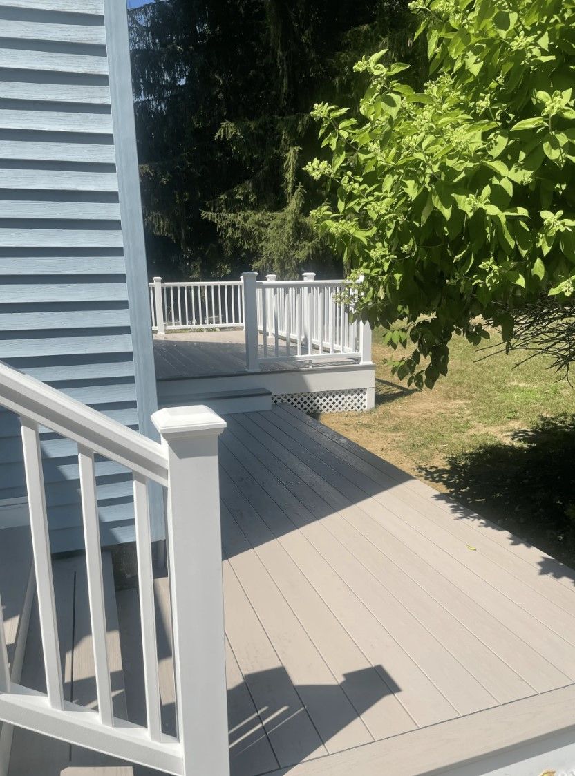 Deck with stairs leading to a higher deck area; light gray decking, white railing, and blue siding.