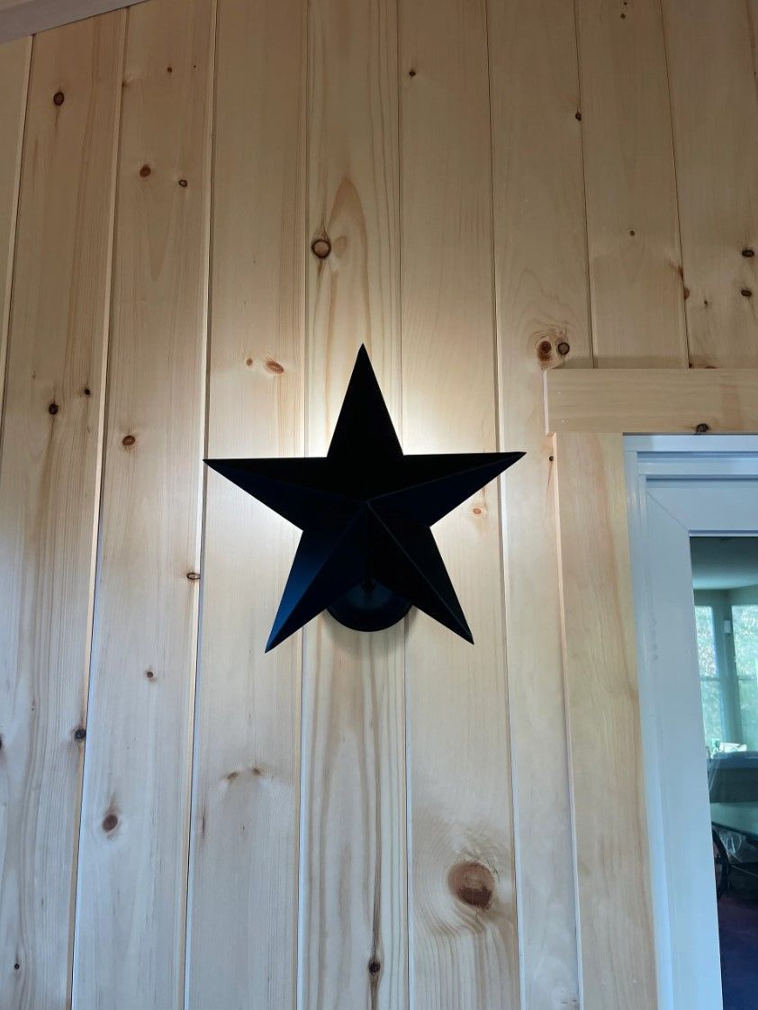 Black star-shaped wall sconce on a light wood paneled wall.