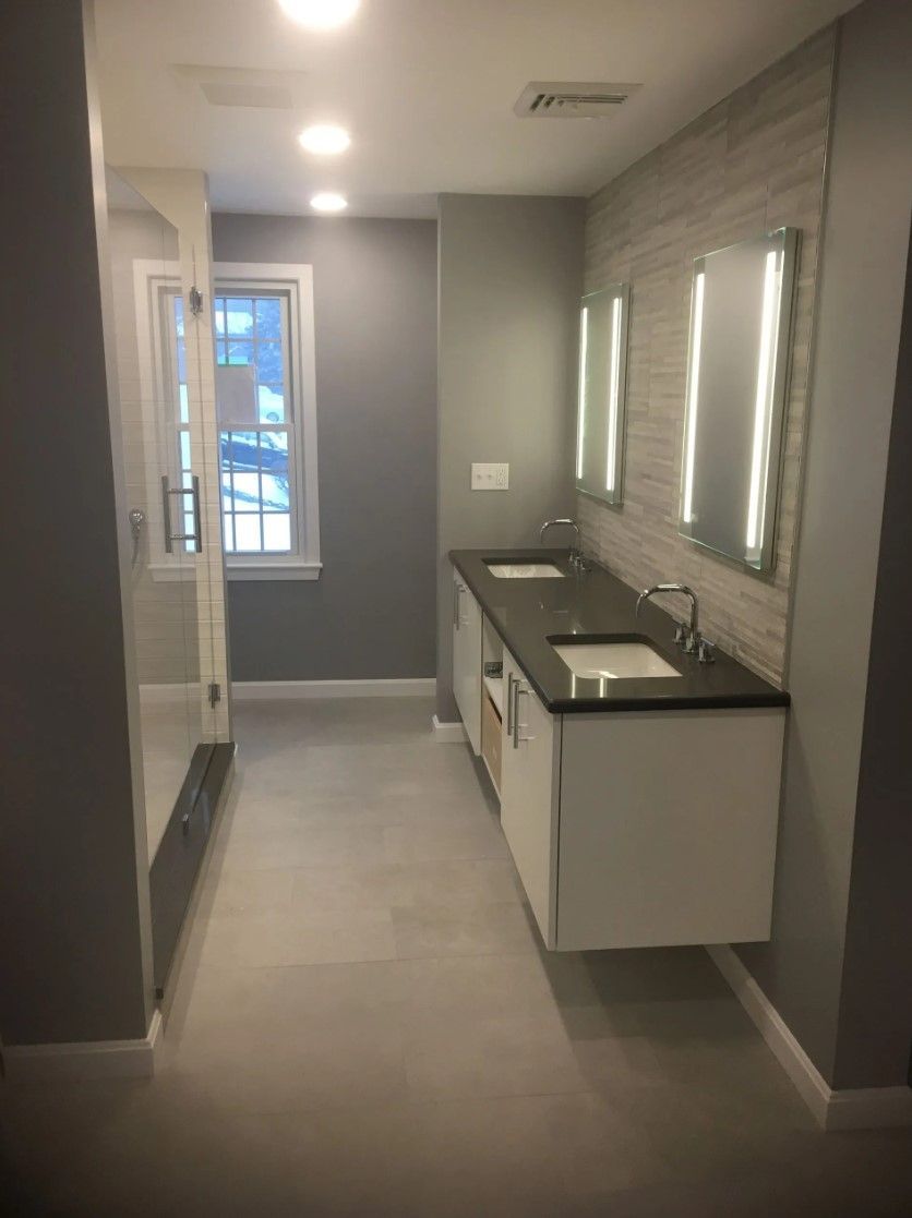 Modern bathroom with gray walls, floating vanity with two sinks, and a glass shower enclosure.
