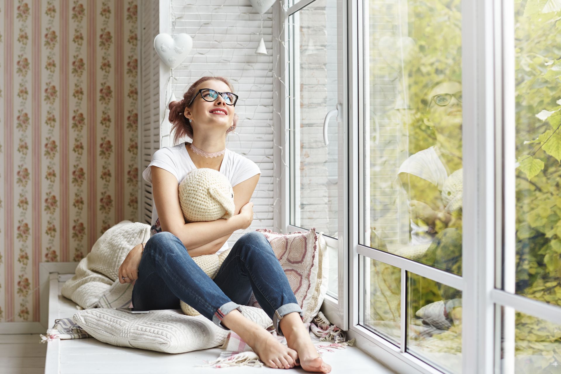 A woman is sitting on a window sill looking out the window.