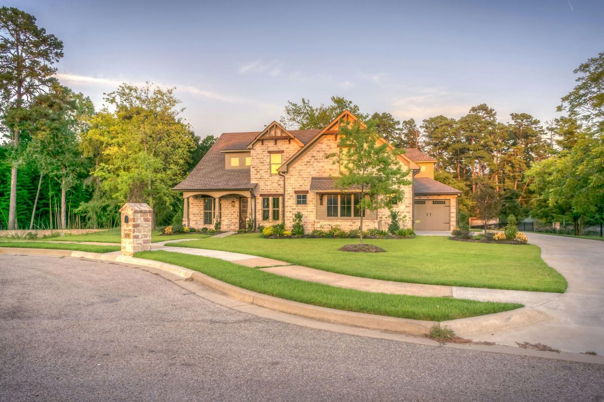 Large stone house with a garage, manicured lawn, and trees at sunset
