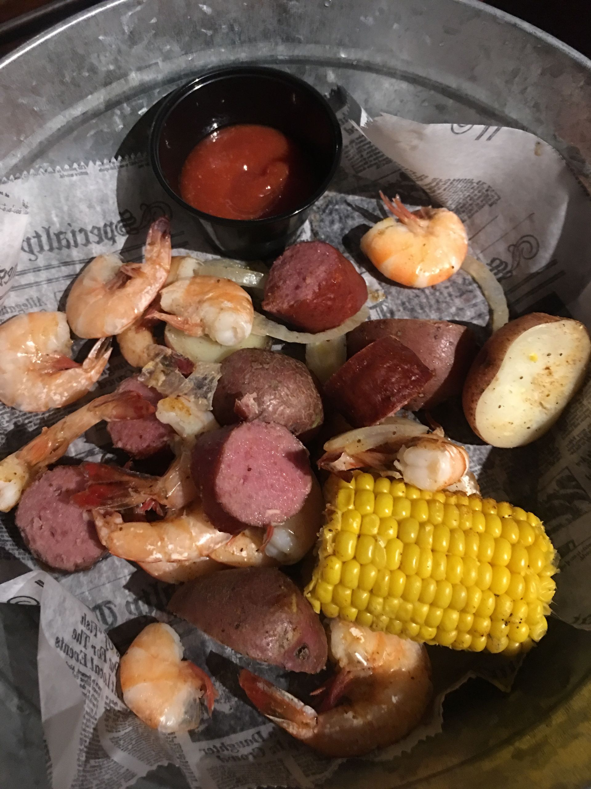 Shrimp boil: shrimp, sausage, potatoes, corn, and dipping sauce in a metal bucket.