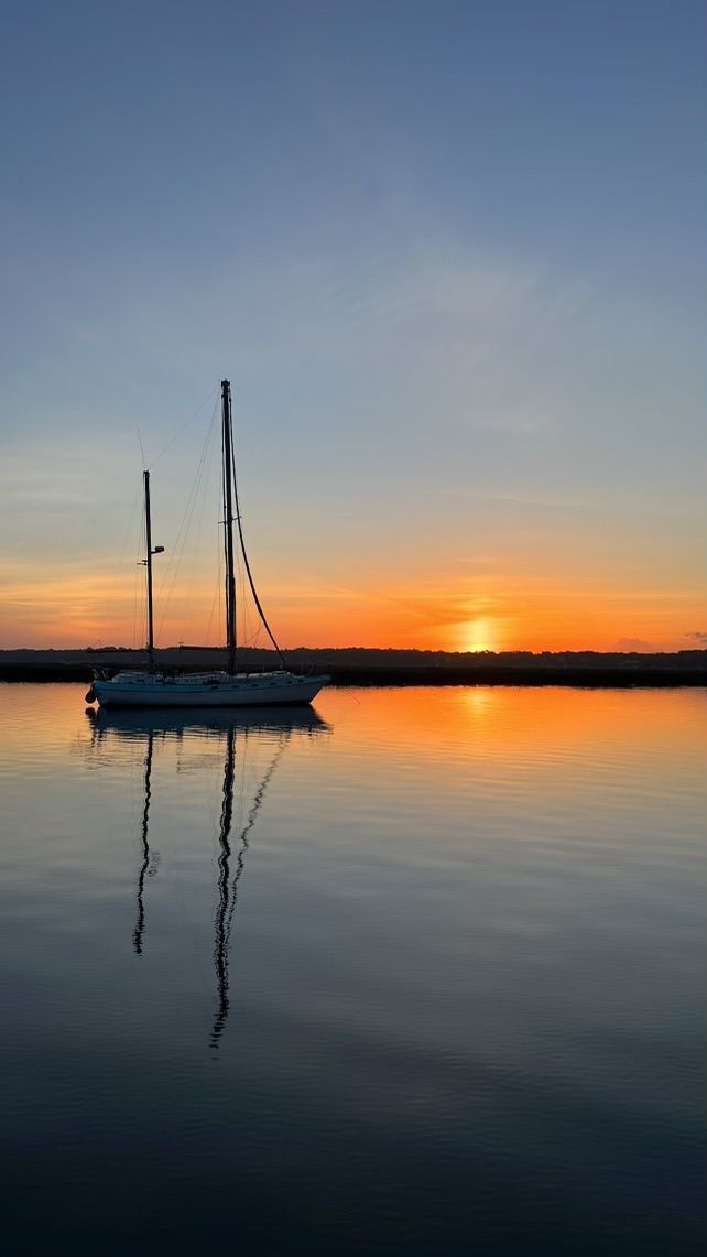 Sailboat on calm water reflecting a colorful sunset.