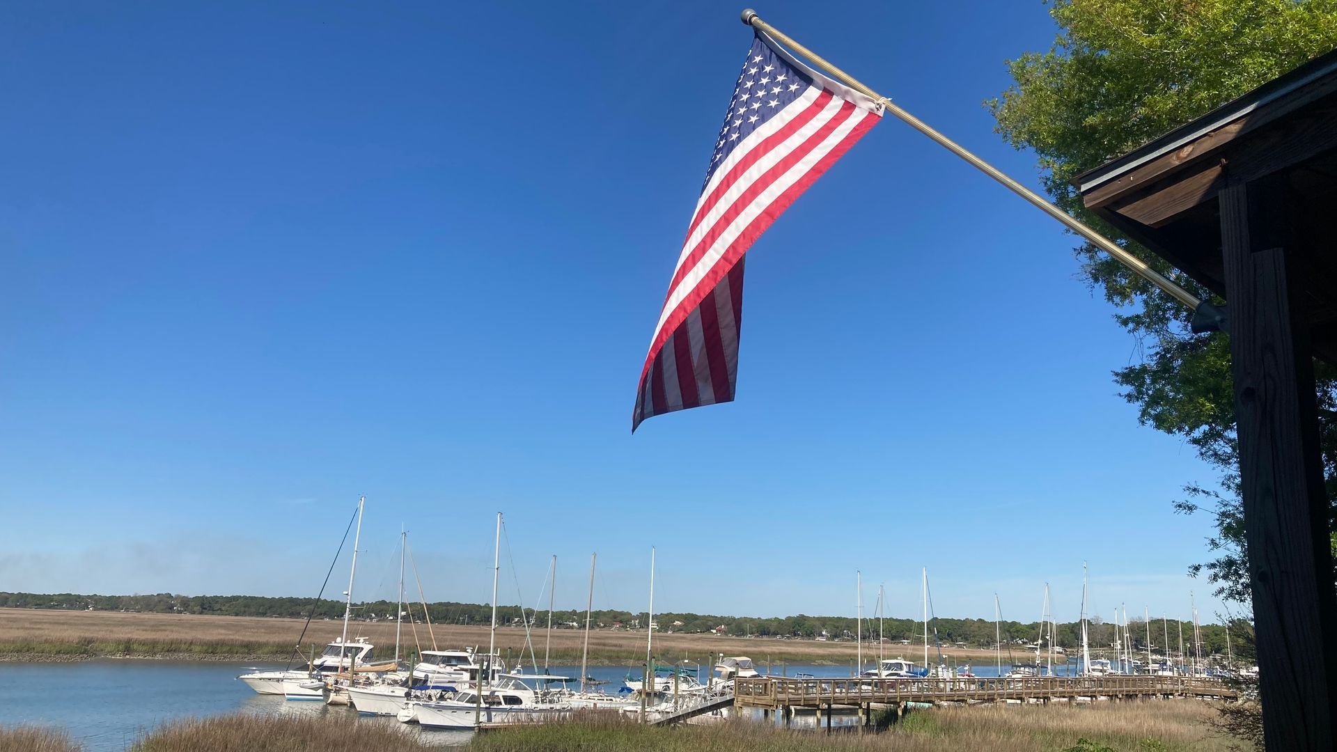American flag flying above a marina with boats on a sunny day.