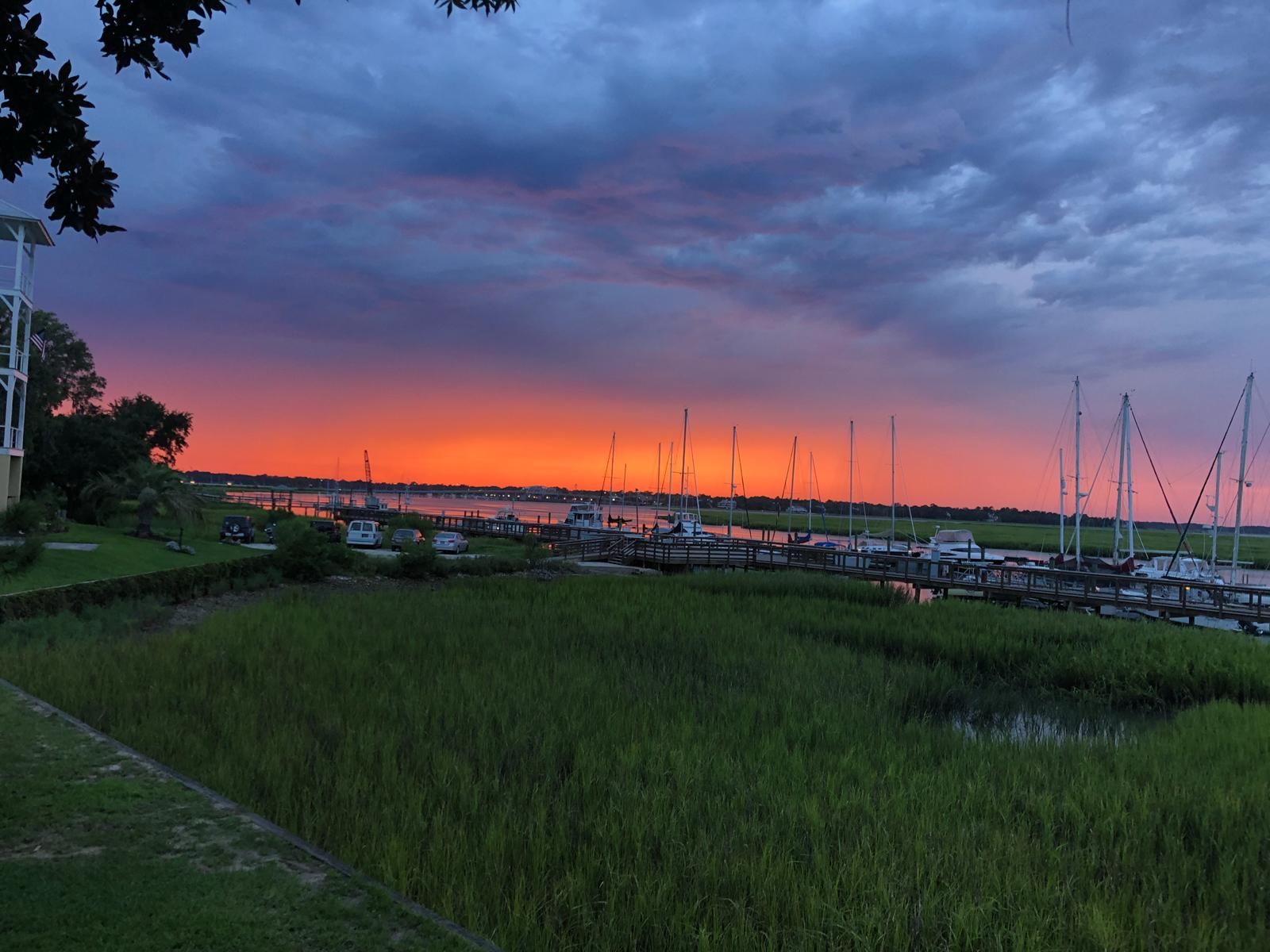 Sunset over Beaufort SC Bay Street marina with boats. Bright orange and purple sky over water and marshy grass.