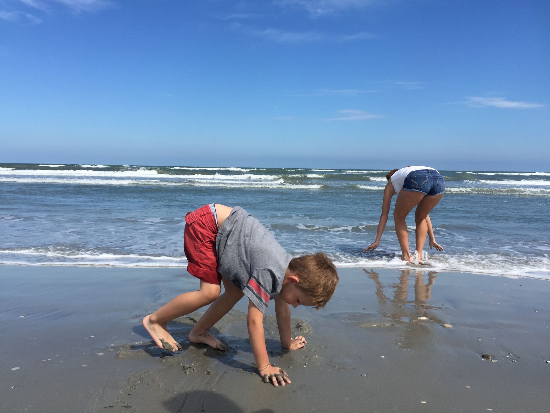 Boy and girl playing on a sandy beach near the ocean; blue sky.