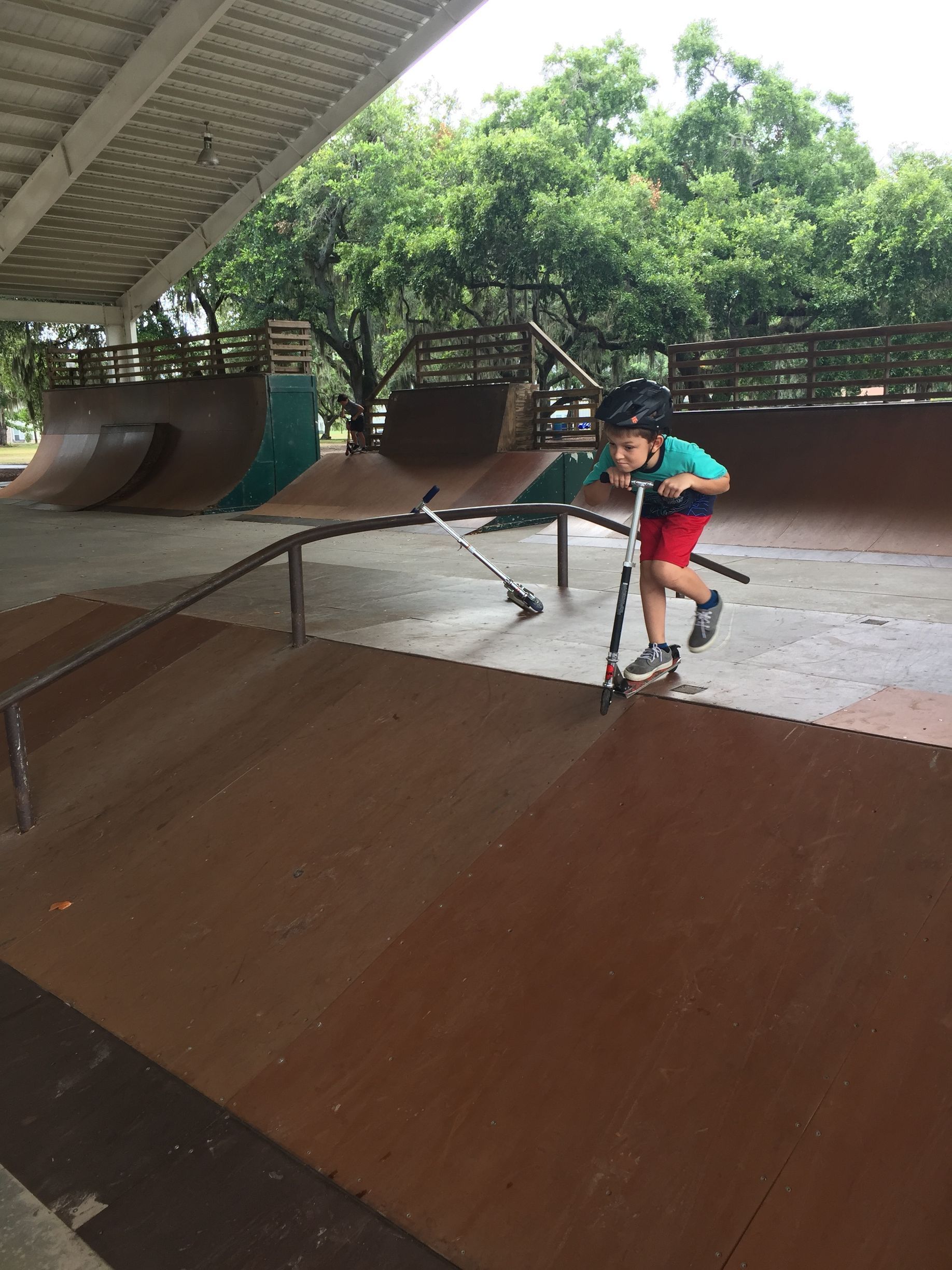 Boy on scooter in skatepark, wearing helmet. He is at the top of a ramp, looking down, ready to go.