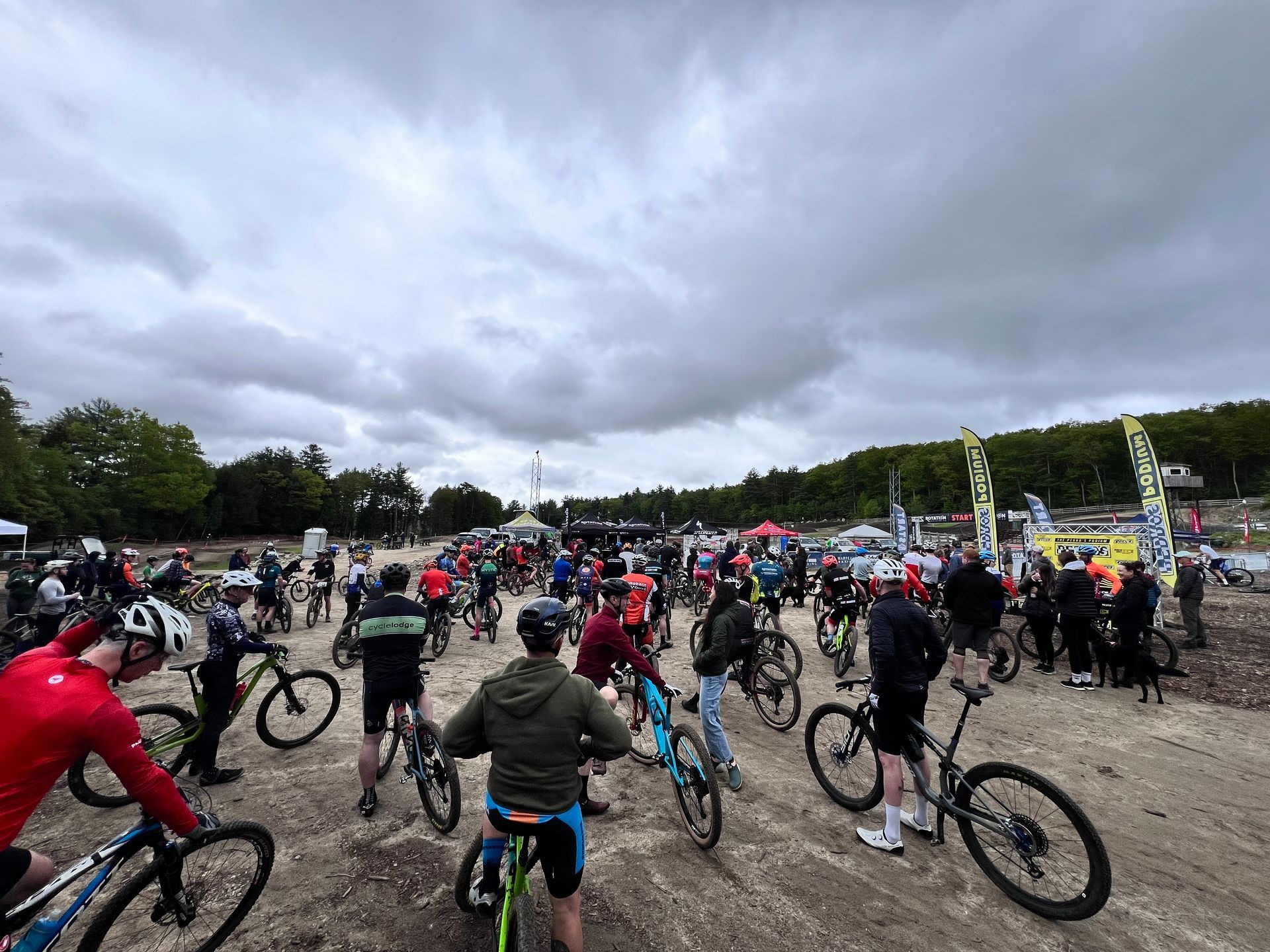Cyclists on bikes at an outdoor event, cloudy sky above.
