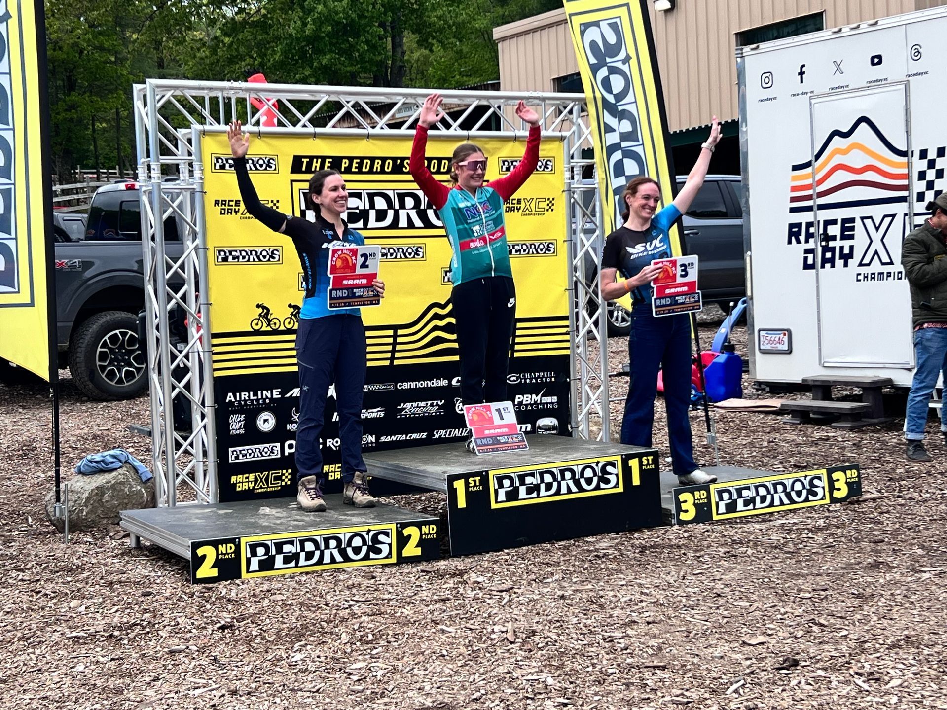 Podium with three men celebrating a competition. One center, arms raised, holding trophy. Others with trophy, arms raised.