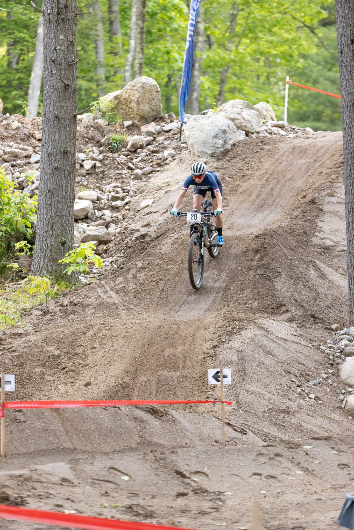 Mountain biker descending a dirt trail in a forest, trees in the background.