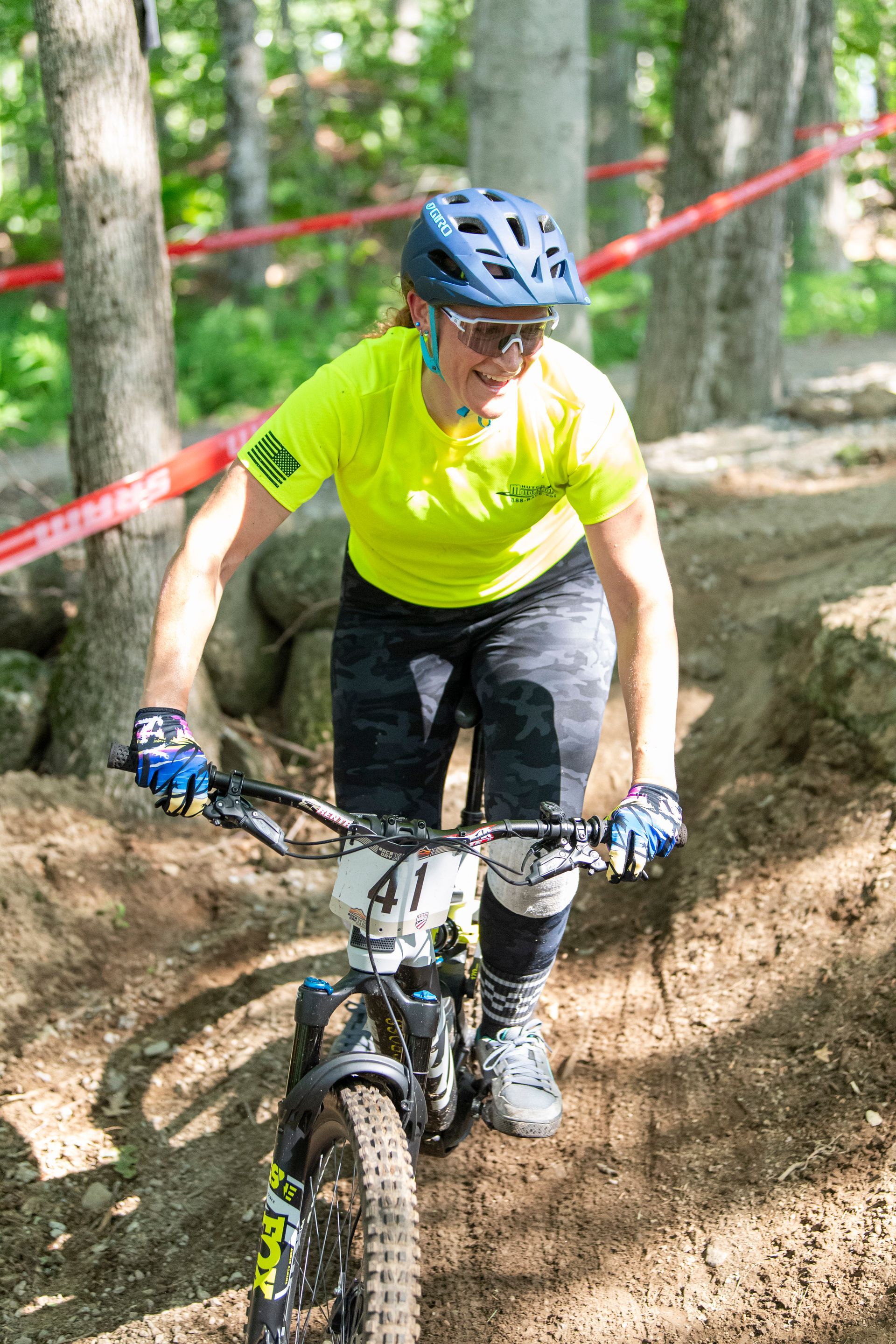 Mountain biker on a trail wearing a yellow shirt and helmet, riding uphill. Forest background.