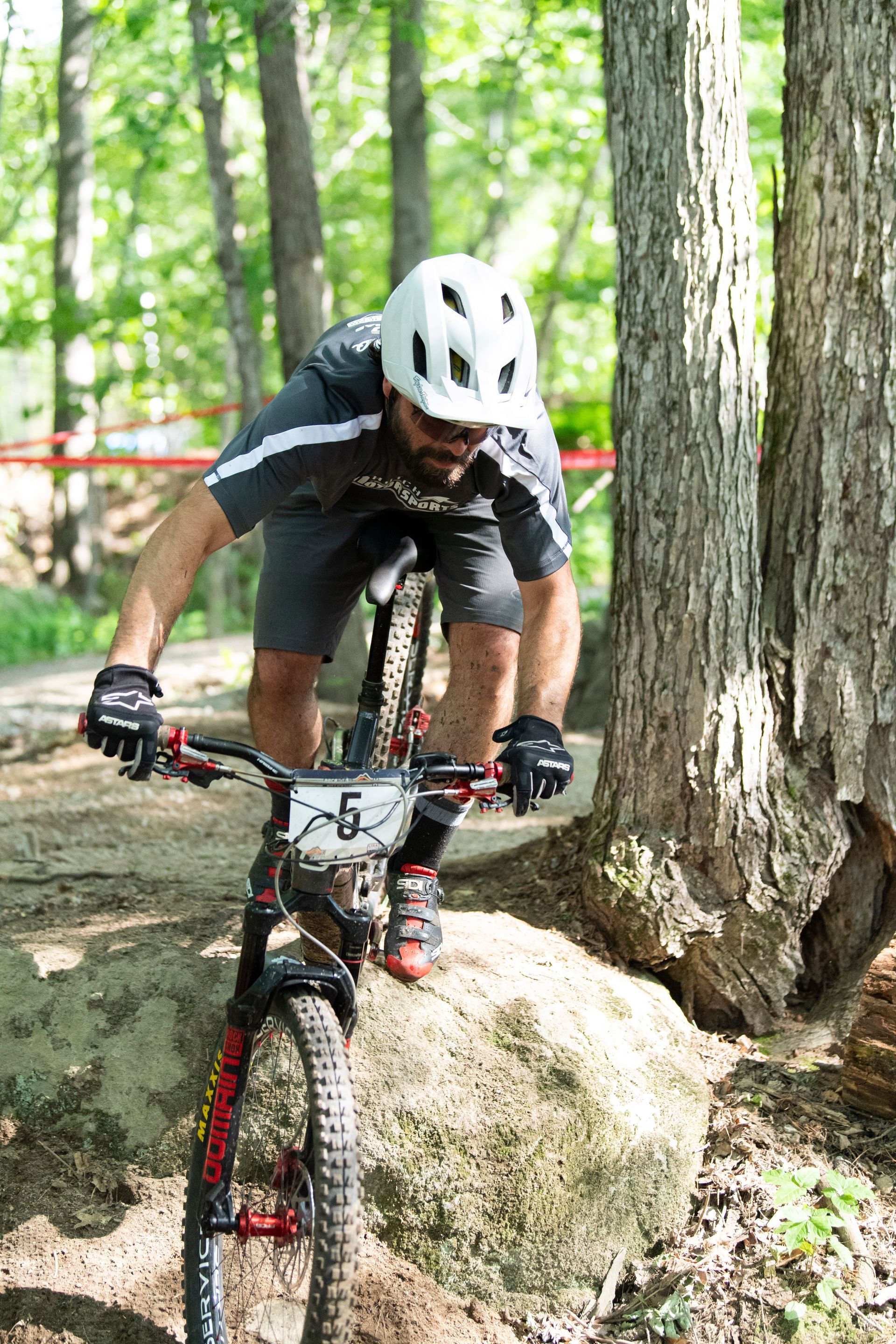 Mountain biker wearing helmet and gloves navigates rocky terrain in a forest.