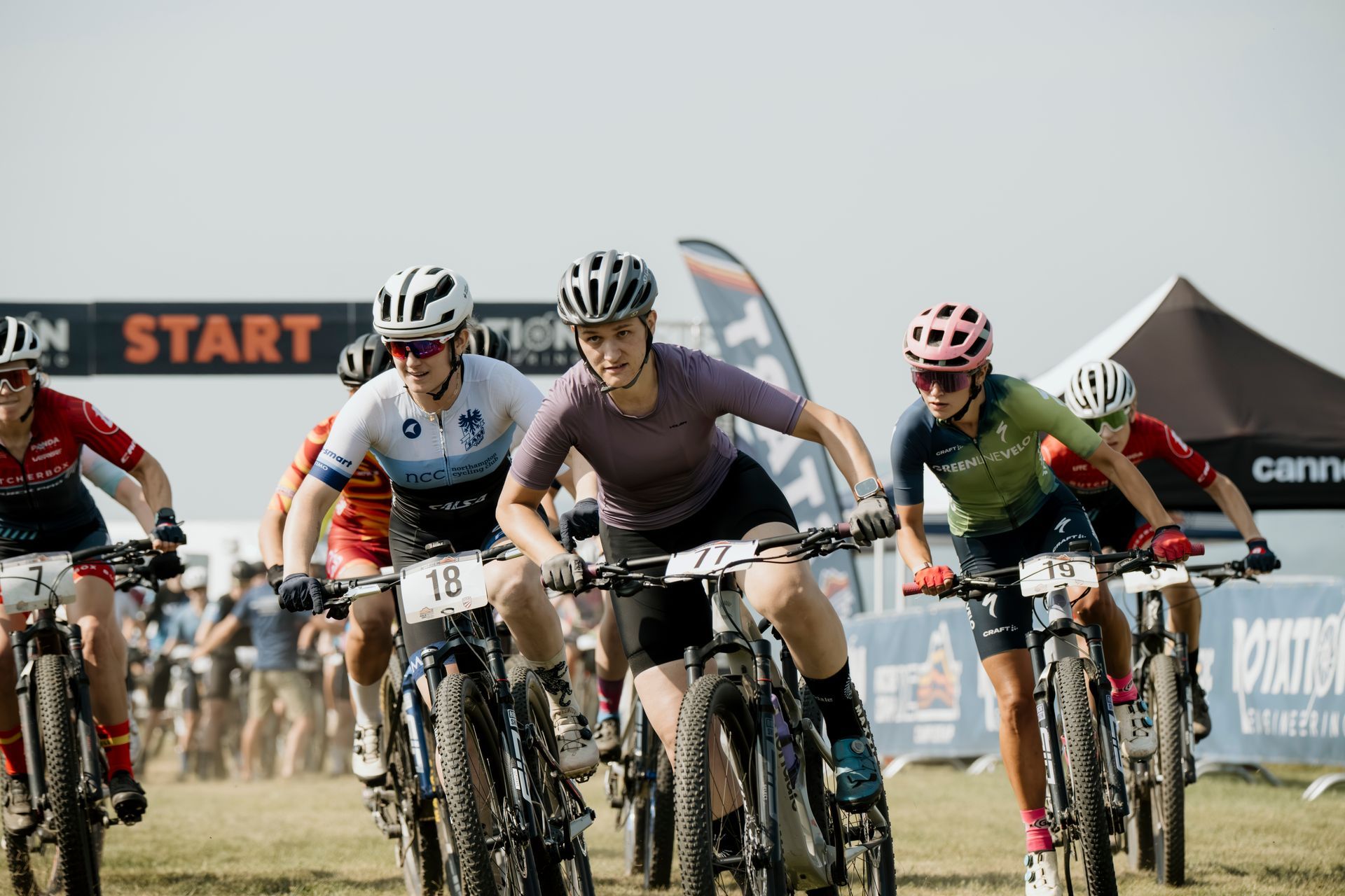 Mountain bike racers at the starting line, ready to compete on a grassy field.