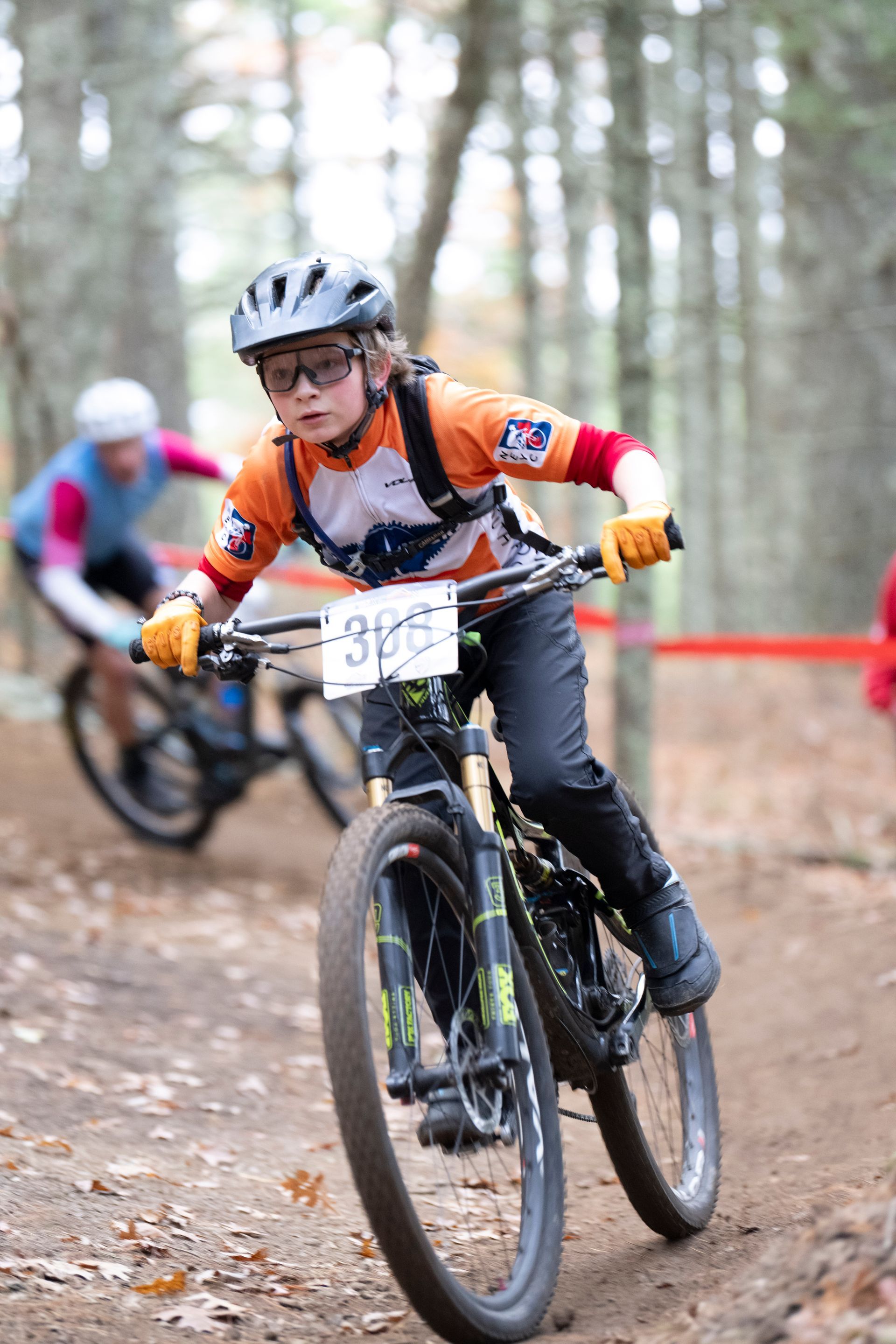 Young cyclist on a mountain bike racing on a wooded trail. Number 396 visible. Orange jersey.