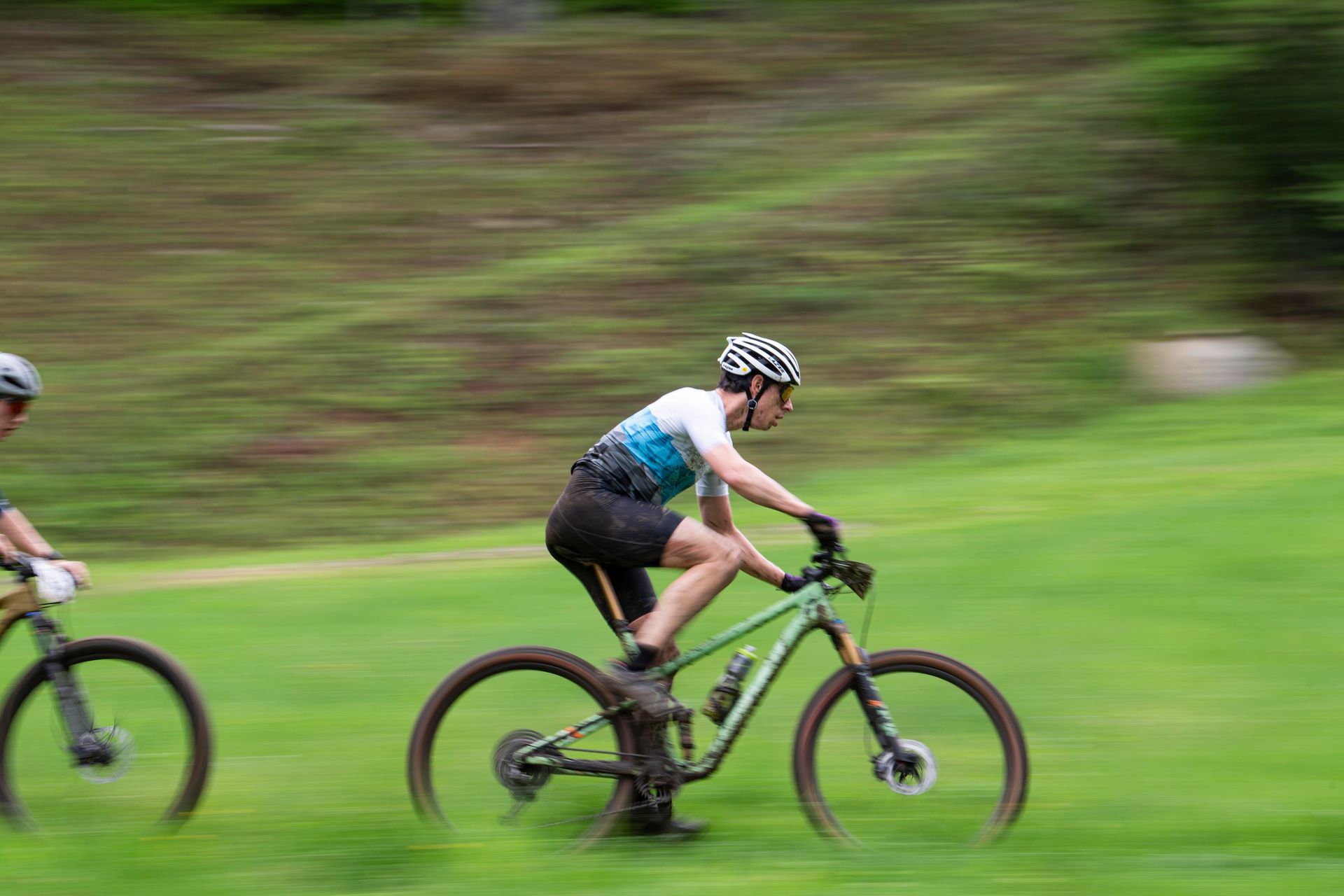 Two mountain bikers riding on green grass, blurred motion.