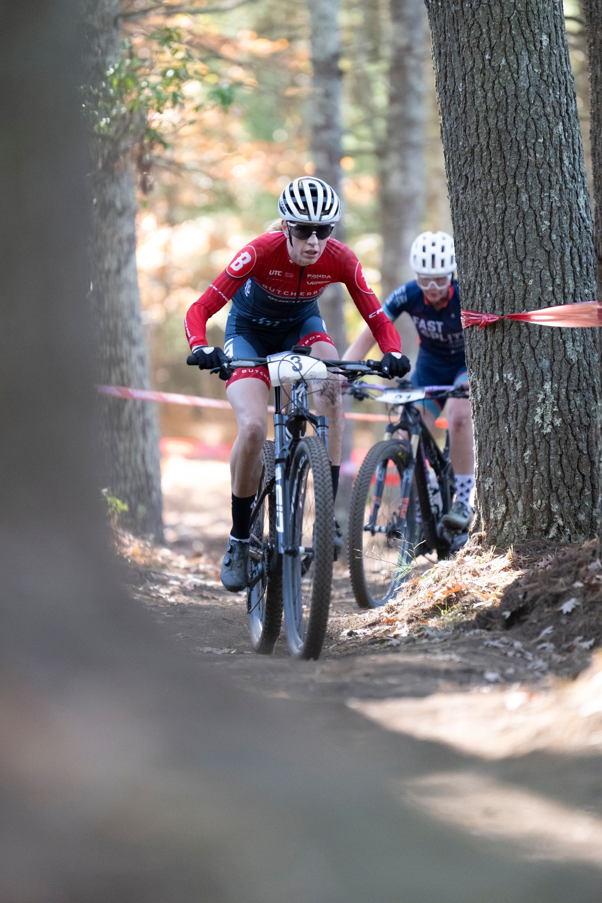 Two cyclists on mountain bikes racing on a dirt trail in a forest.