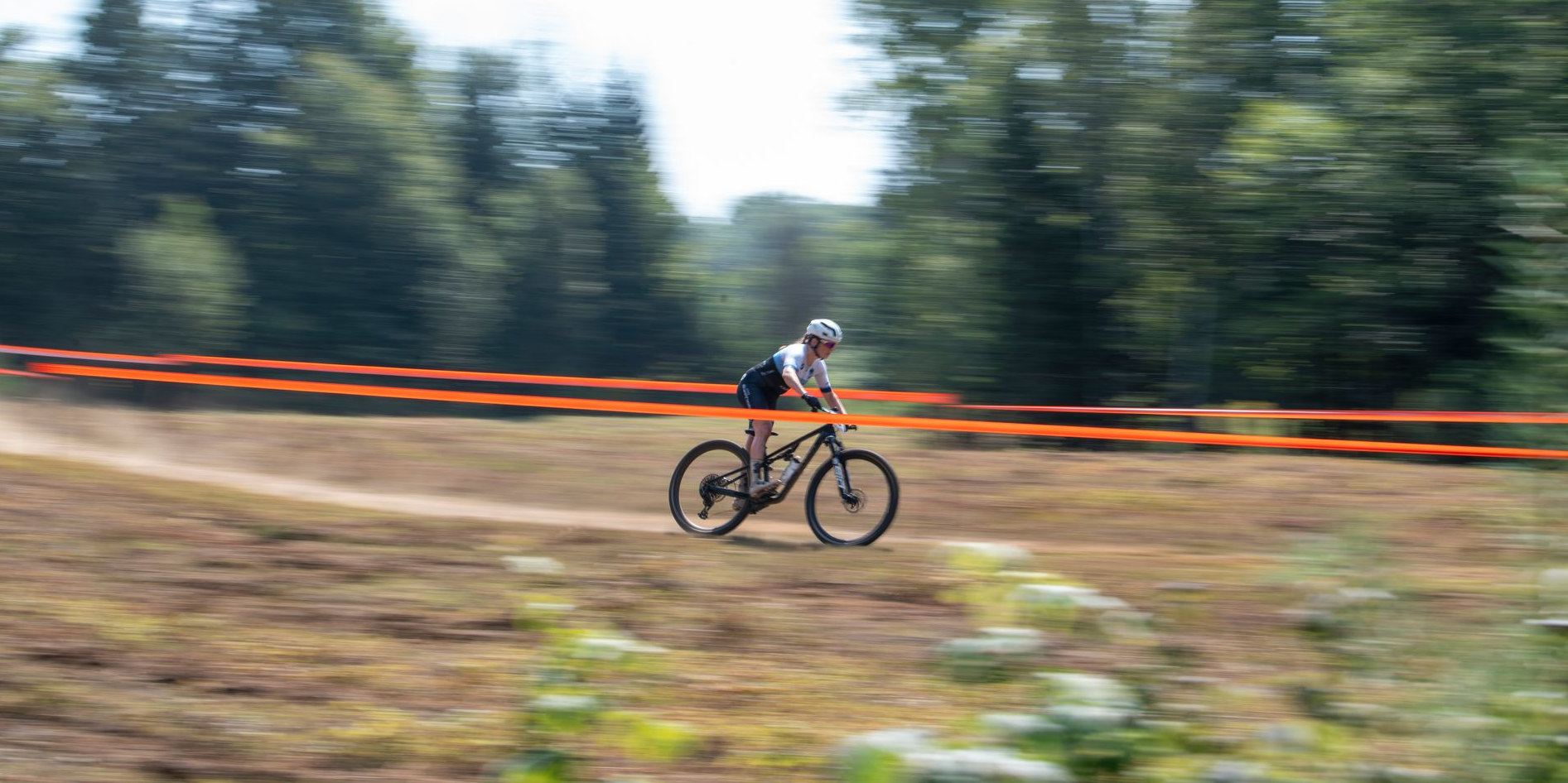 Cyclist on mountain bike rides on dirt path, trees in background.