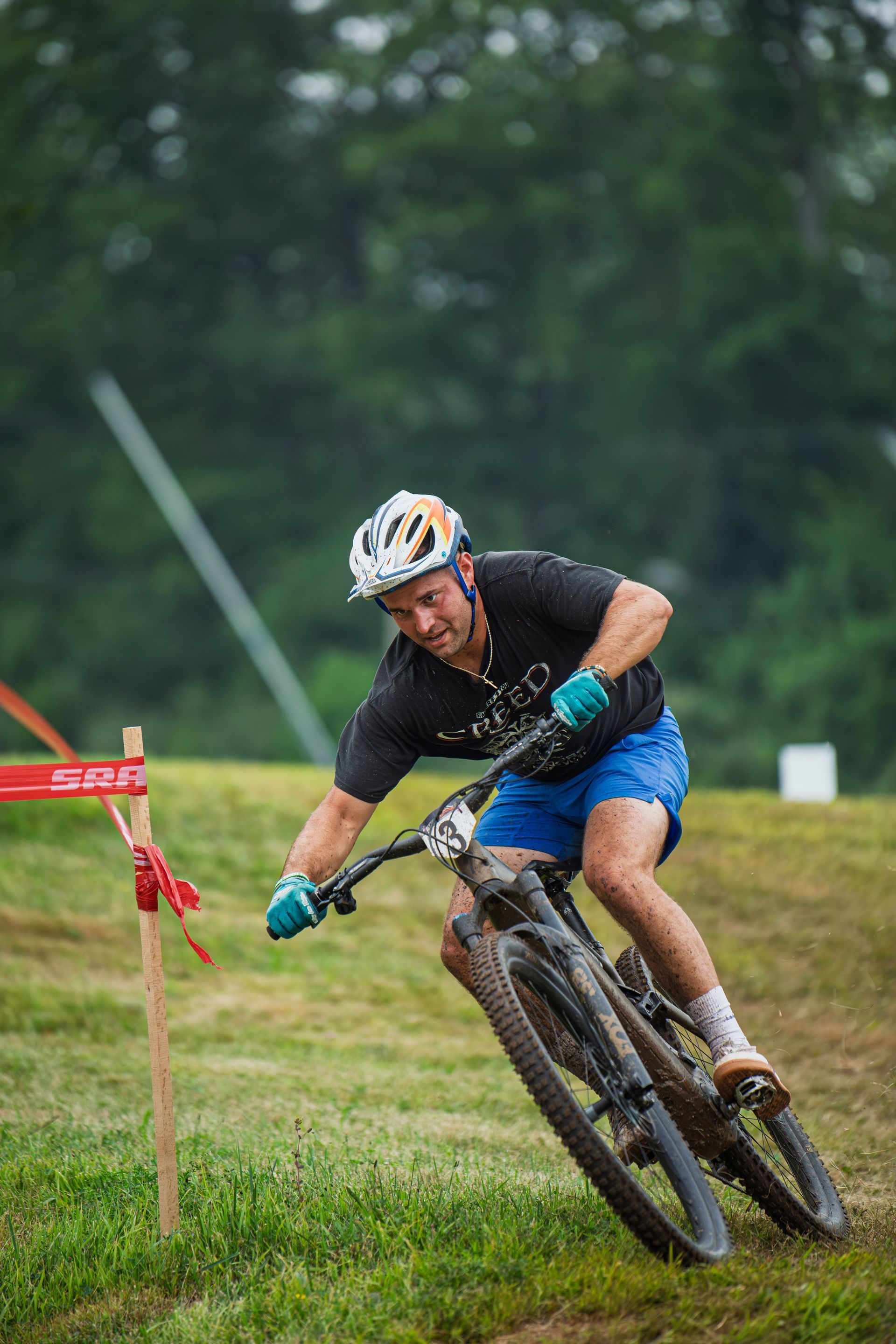 Mountain biker leans into a turn on a grassy course, wearing a helmet and blue shorts.