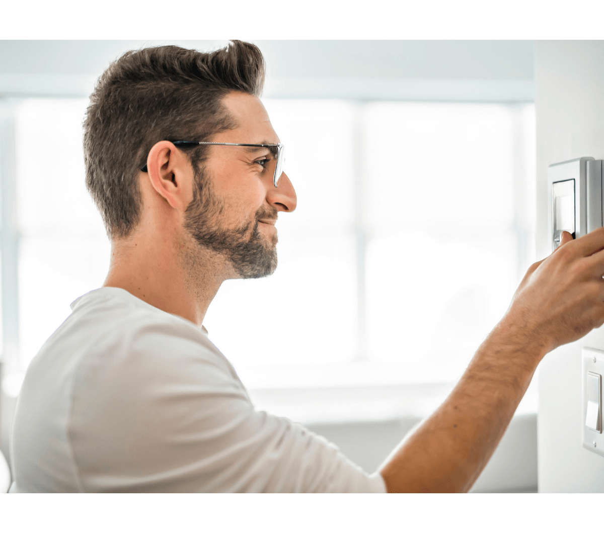 man with glasses adjusting thermostat. 