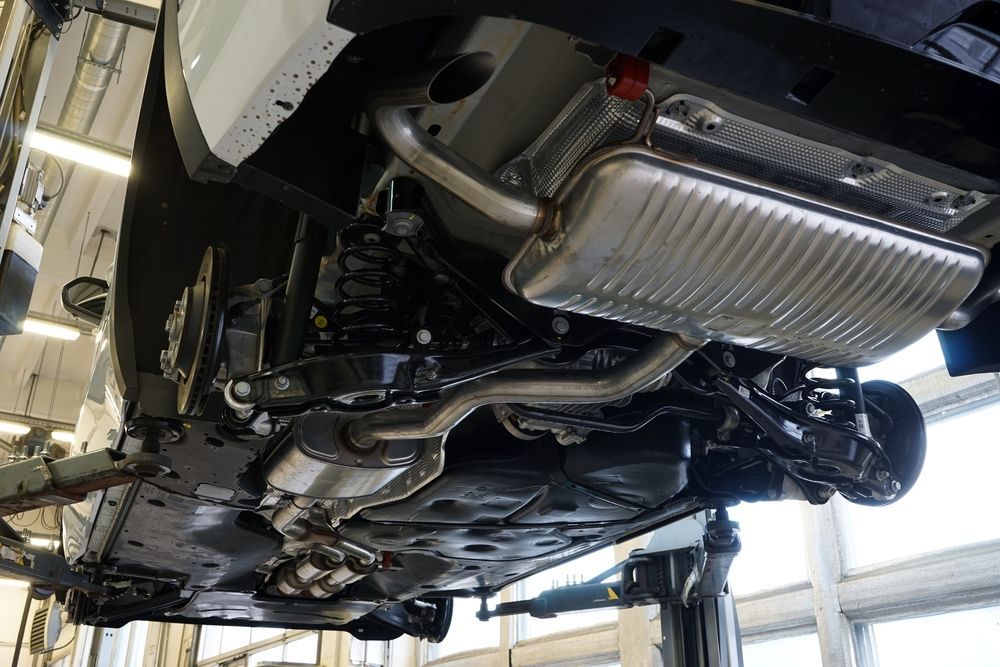 Underside of a car on a lift showing the exhaust system and suspension components.