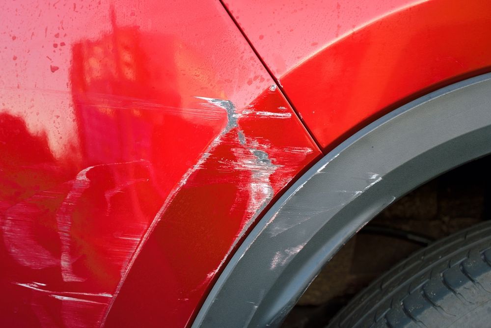 Red car with significant scratches and damage near the wheel well.
