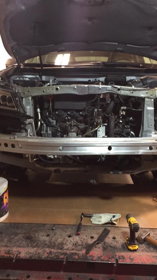 Car with open hood, front end disassembled, revealing engine components. Tools on a table in front.