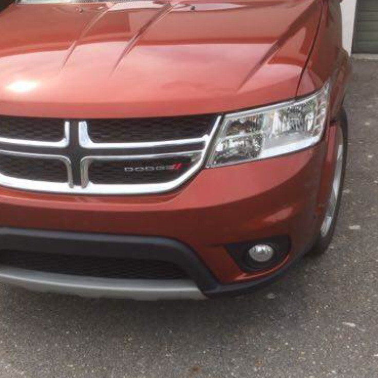 Orange Dodge Journey SUV front view, with Dodge logo on grill.