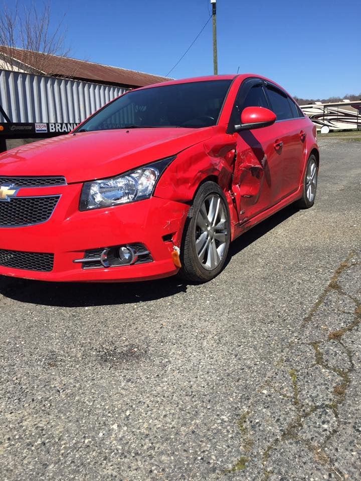 Red Chevrolet Cruze with significant damage to the front driver's side, parked on gravel.