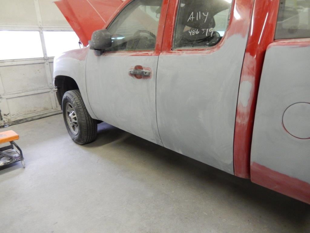 Red and gray pickup truck undergoing body repair in a garage. Doors are prepped for paint.