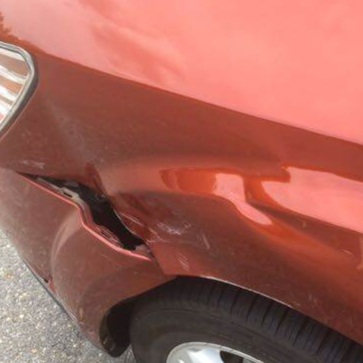 Damaged orange car fender with significant dent and split near the front wheel.