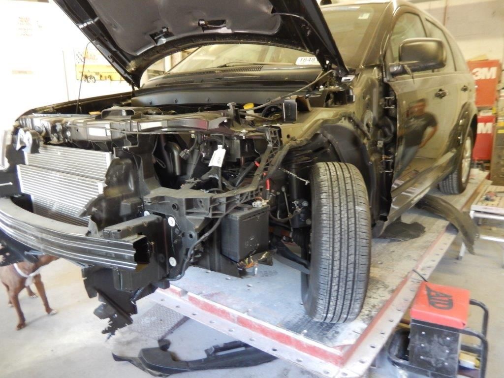 Black SUV with open hood undergoing front-end repair on a lift. Shop environment.
