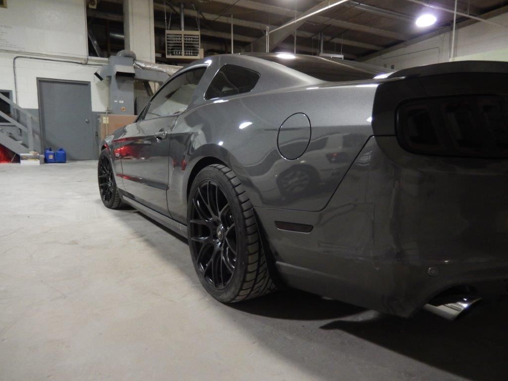Dark gray Mustang car with black wheels in a garage.