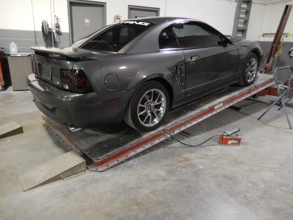 Dark gray Ford Mustang on a vehicle lift in a garage, angled view.