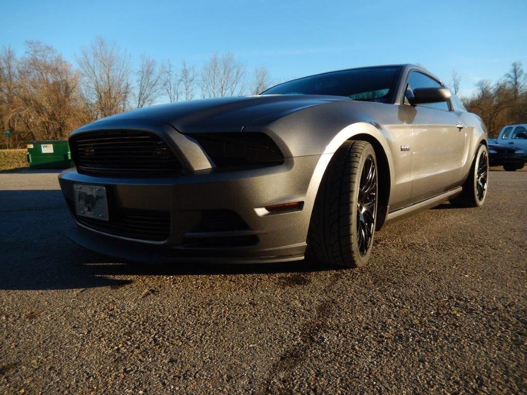 Gray Ford Mustang parked on gravel. Black wheels, tinted windows. Sunny day.