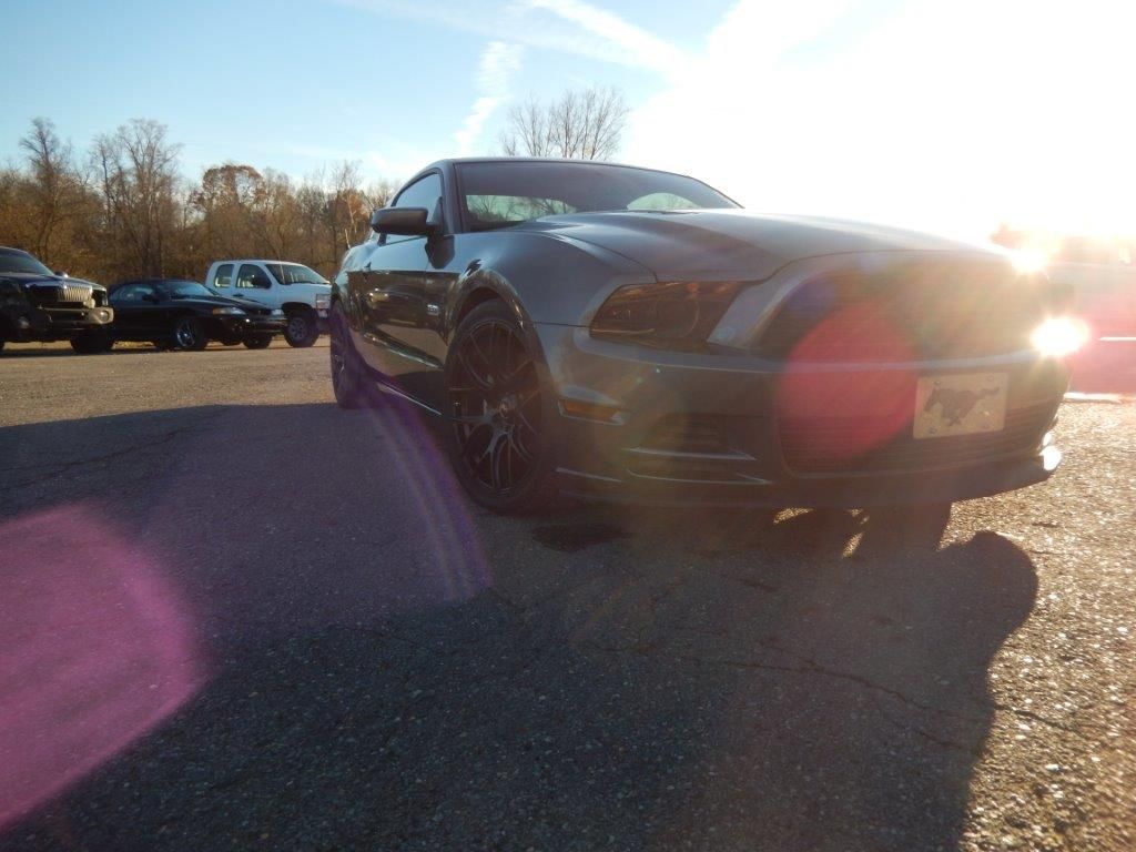 Dark gray Ford Mustang parked on asphalt, sunlight shining from the right.