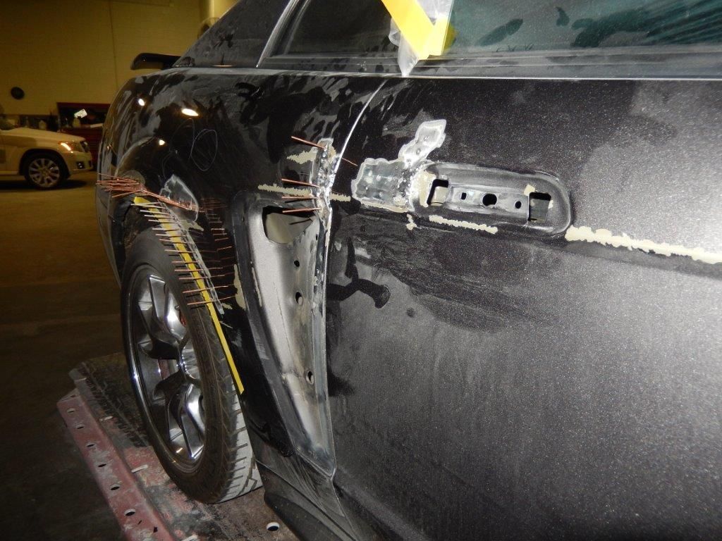 Damaged black car door at a repair shop, showing bodywork and missing door handle.
