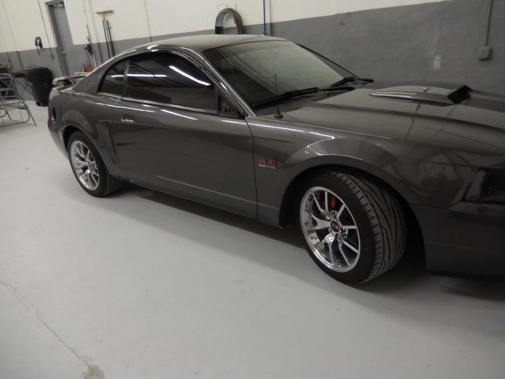Gray Ford Mustang coupe with chrome wheels in a garage.