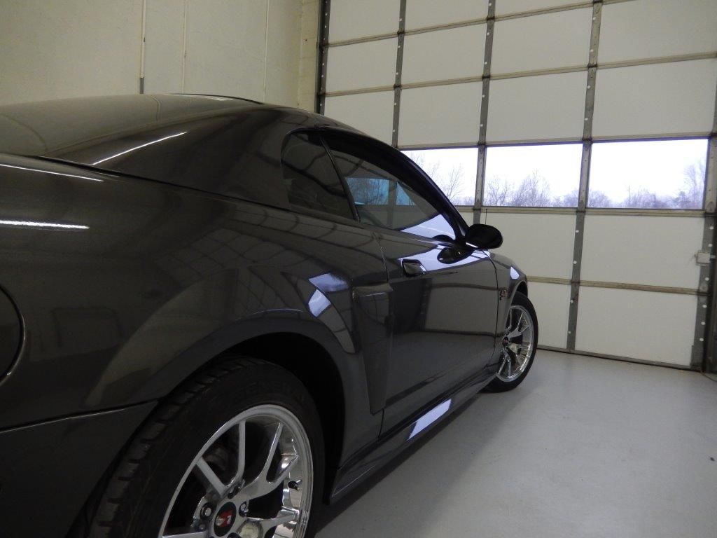 Dark gray Mustang sports car parked in a garage with a white door.