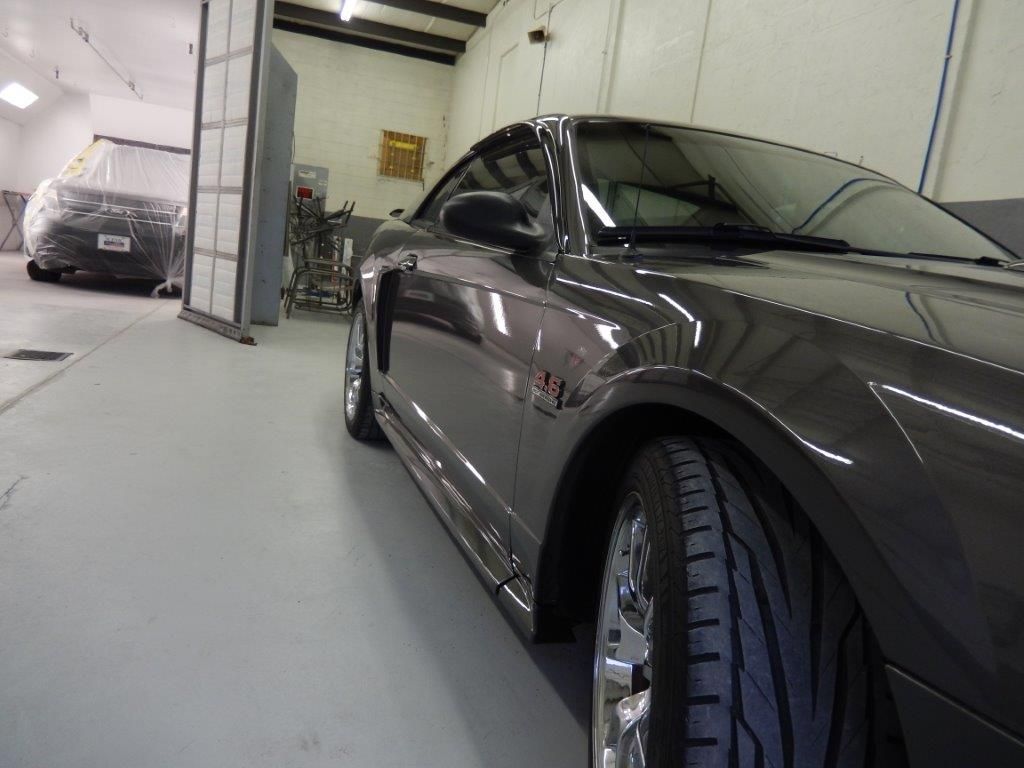 Dark gray Mustang in a shop. Another car is covered in the background.