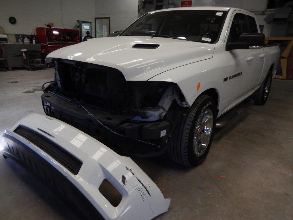 White Dodge Ram pickup truck with the front bumper detached in a repair shop.