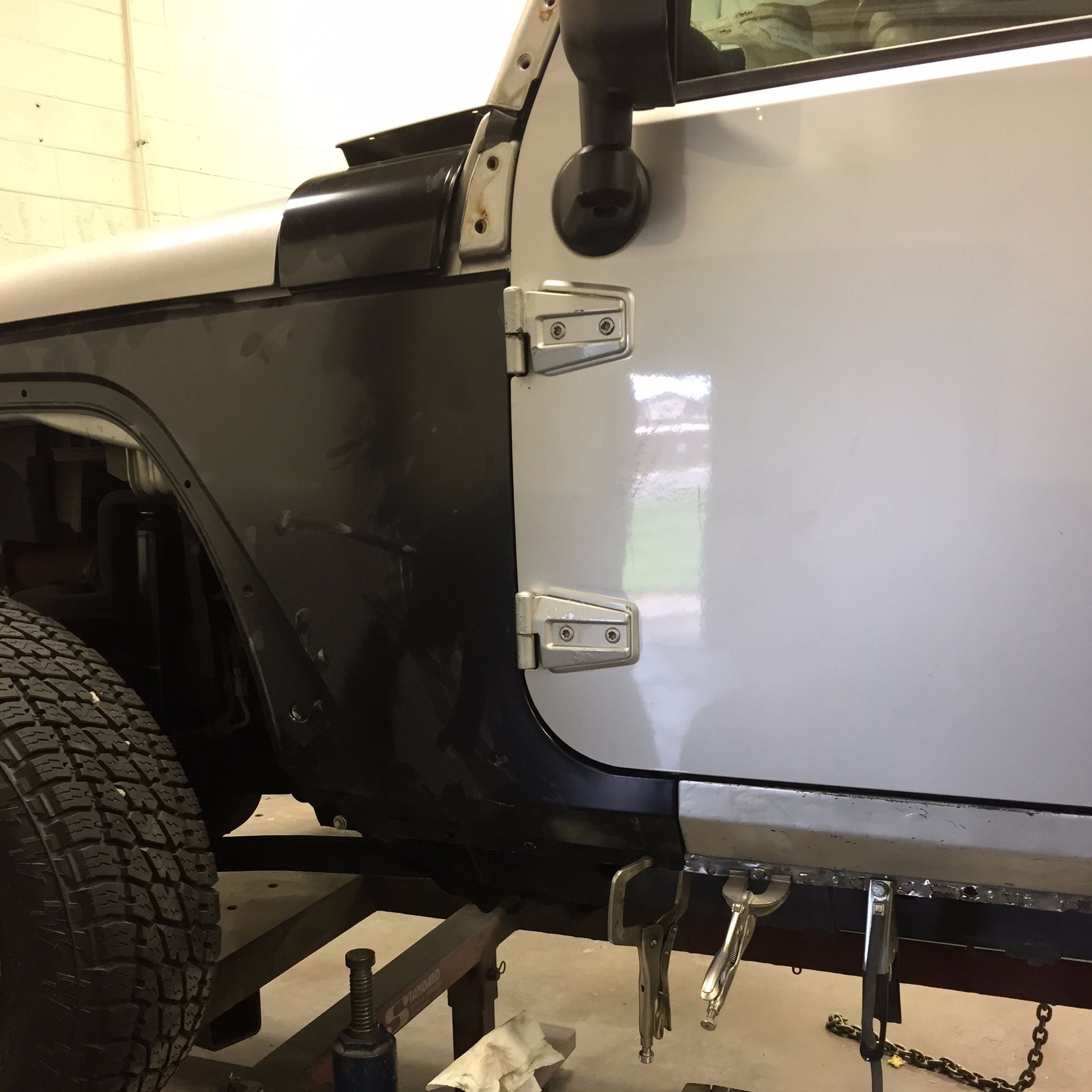 Silver Jeep being repaired; the side panel is black with a silver door.