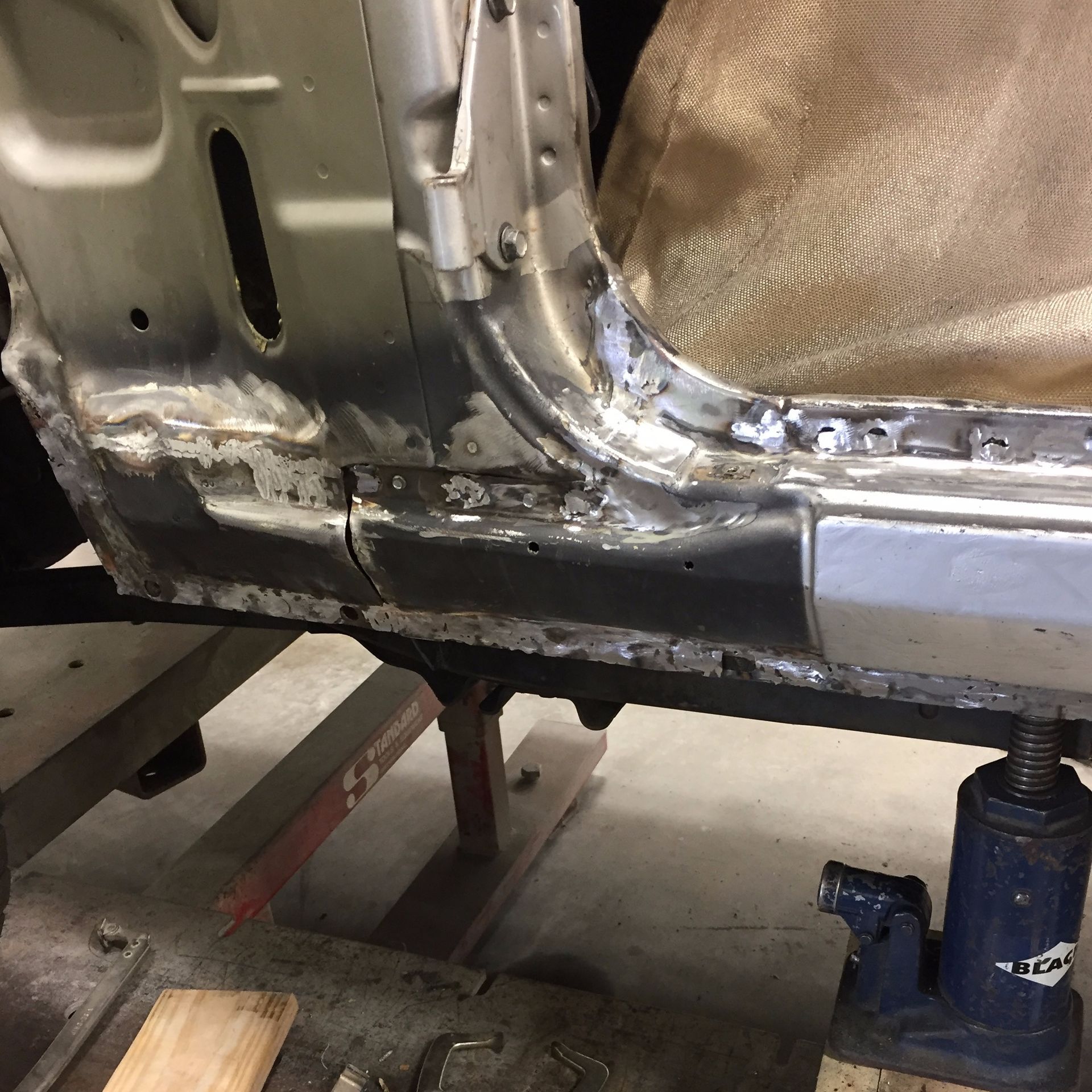 Car frame undergoing repair; metal welding and bodywork in progress.