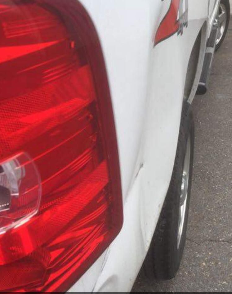 Damaged white truck rear quarter panel with taillight and dent.
