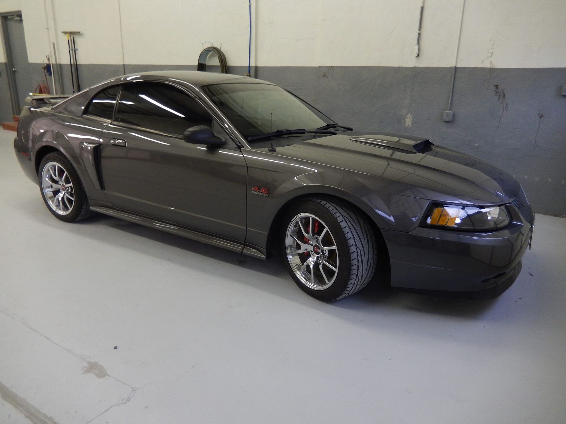 Dark gray Ford Mustang coupe with chrome wheels in a garage setting.