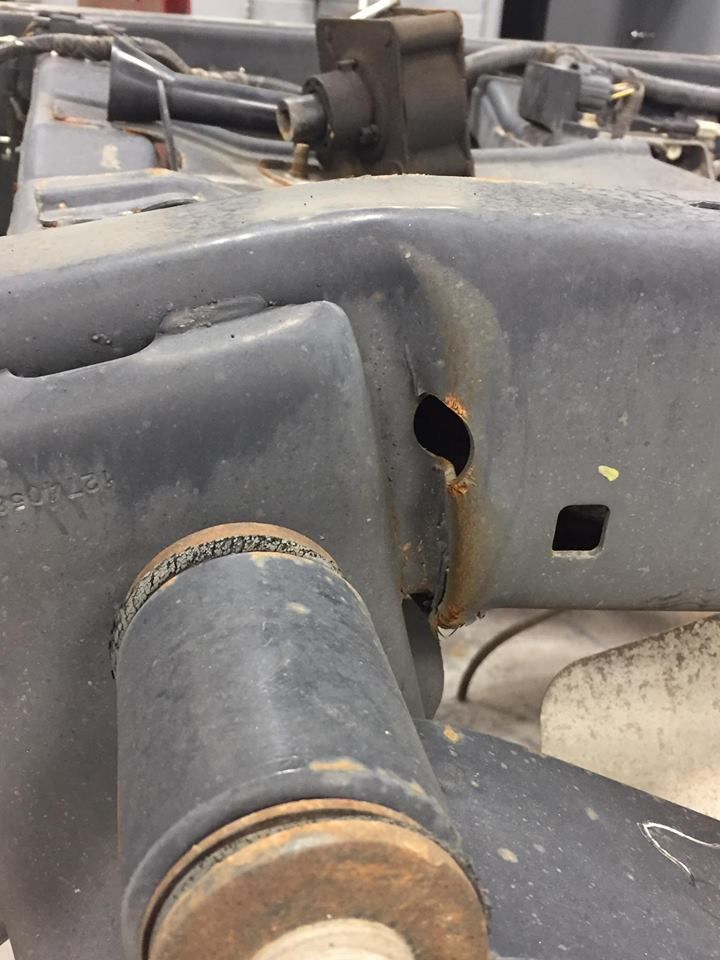 Black truck frame with rust damage around a hole.
