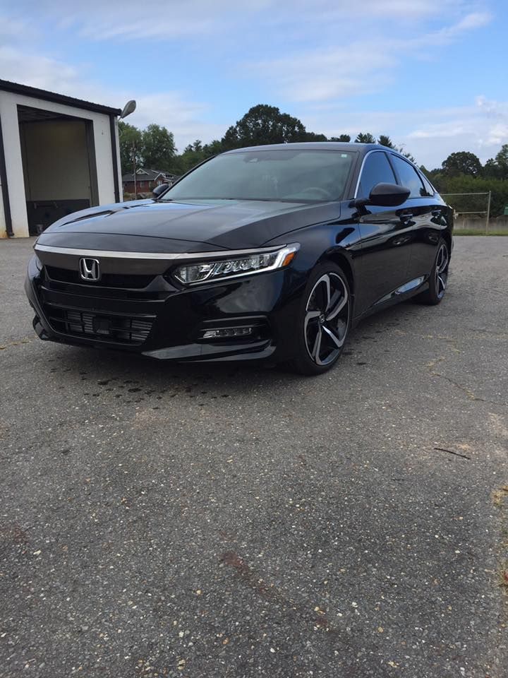 Black Honda Accord sedan parked on asphalt. Building and trees in the background.