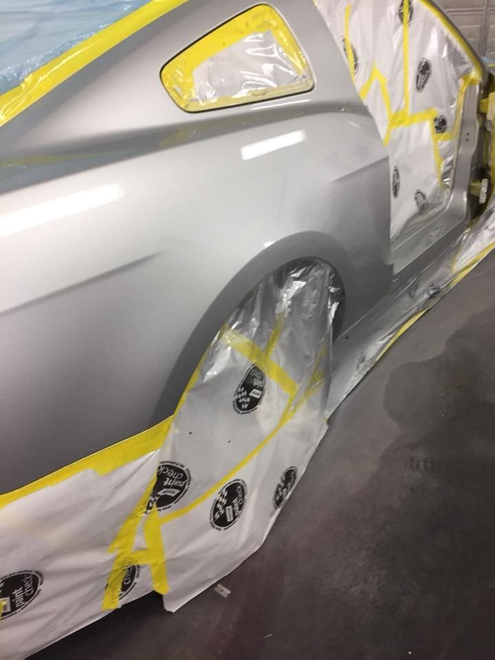 Silver car being painted in a workshop, masking tape and plastic covering sections.
